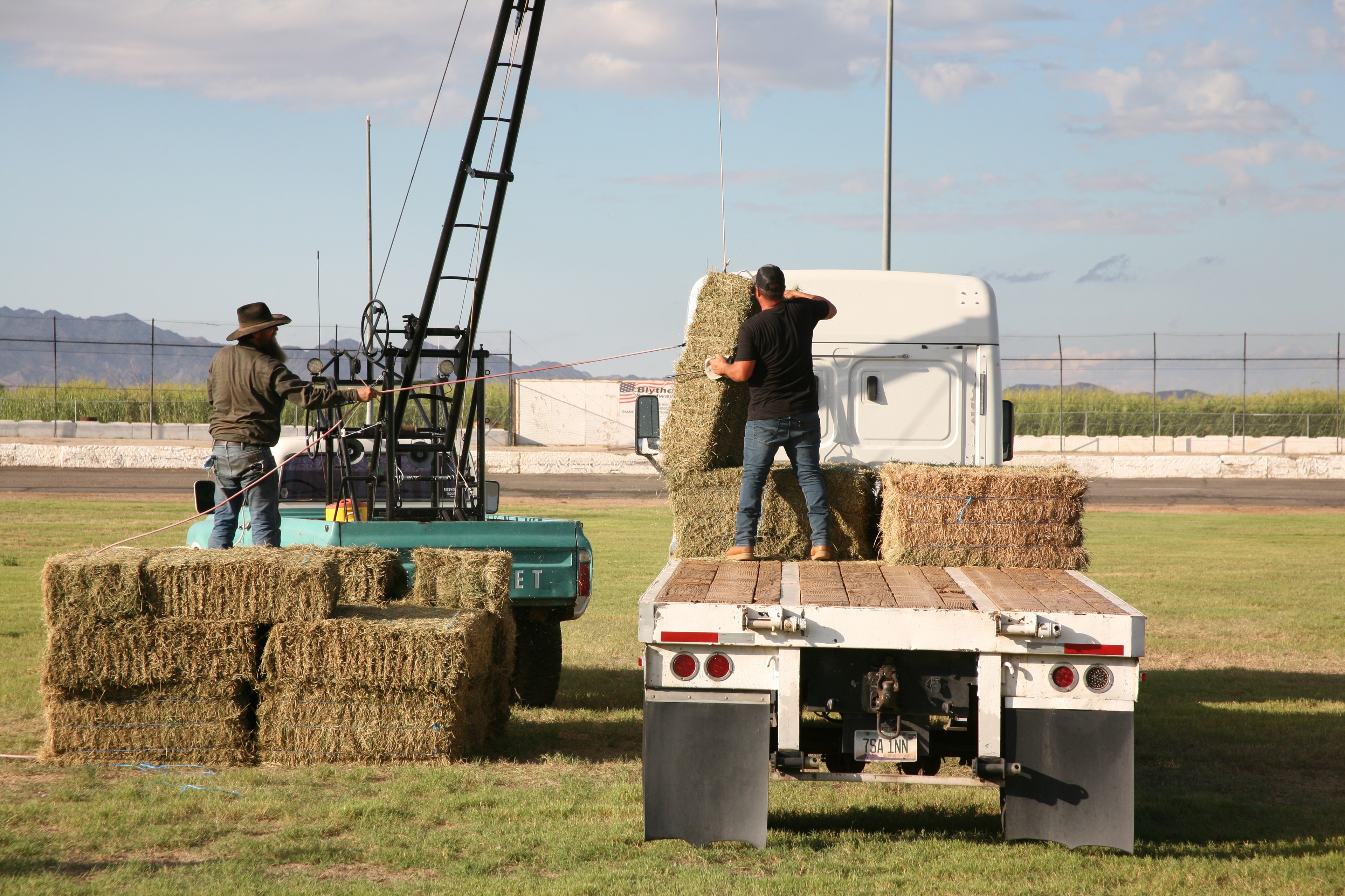 Competitors loading hay bales onto a flatbed truck using a boom crane